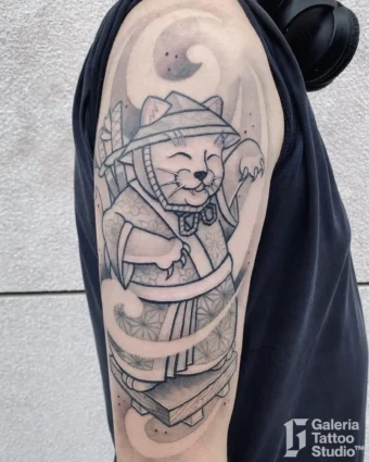 Linearny cartoonowy tatuaż kota w azjatyckim stroju na przedramieniu: biały Maneki-neko z kapeluszem, kijem, kimonem, yin-yang i uśmiechniętą, machającą łapką miną.